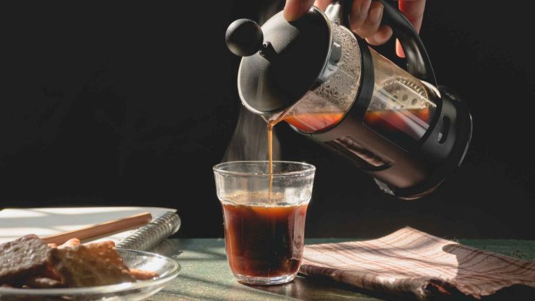 A French press coffee maker and a mug on a wooden kitchen counter.
